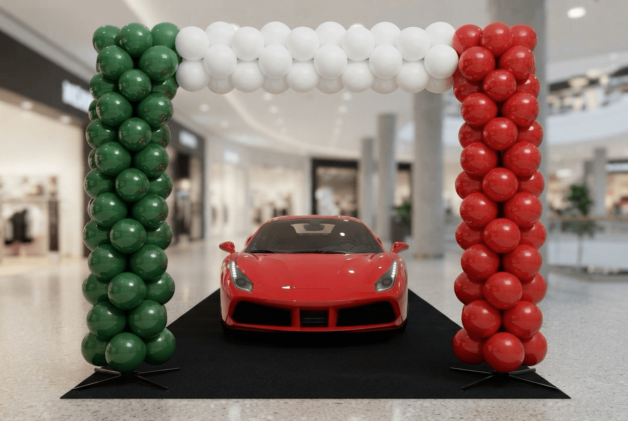 Ballonsäulen in Grün, Weiß und Rot mit einem Bogen darüber um einen roten Sportwagen im Showroom