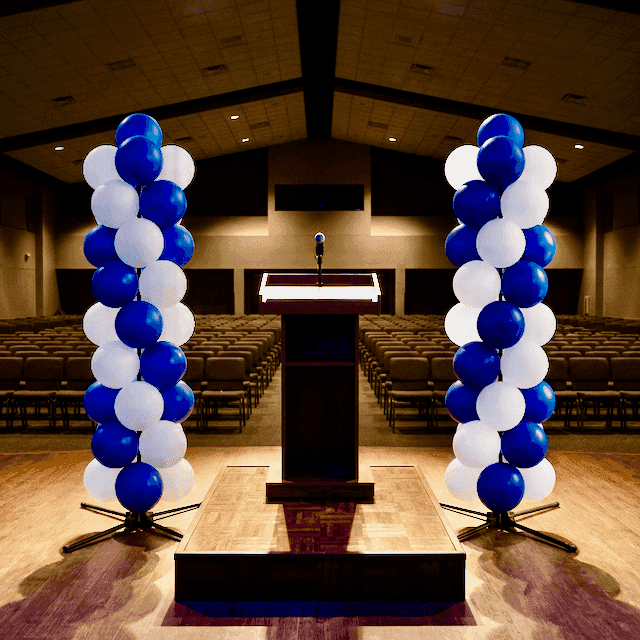 Professionelle Ballonsäulen in Schulfarben bei Abschlussfeier in einer festlich beleuchteten Aula